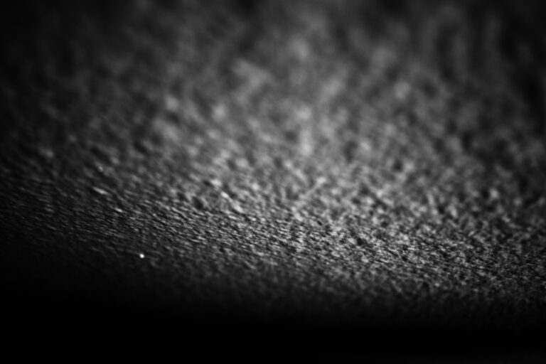 Abstract black and gray photographic texture with shallow depth of field, granular surface fading into darkness, original photograph by ACFA Creative House